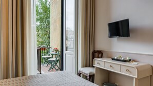 Una habitació d'hotel amb un llit, un escriptori amb calaixos, un televisor fixat a la paret i un balcó amb taula i cadires.