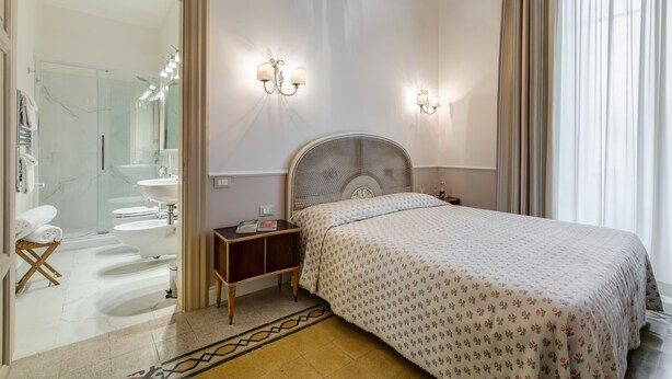 Une chambre à coucher comprenant un lit, des tables de chevet, une commode, un miroir et une salle de bain visible à travers une porte ouverte.