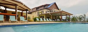 A hotel with a swimming pool, lounge chairs, and a covered outdoor area.