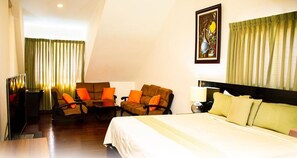 A hotel room with a bed, two armchairs, a desk, and a painting on the wall.