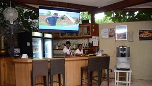 A bar area with a TV screen, bar stools, a refrigerator, and a water dispenser. - Elite Hotel (Port-au-Prince)