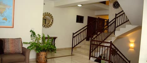 A hotel lobby with a staircase, a sofa, a coffee table, a potted plant, and a wall map.