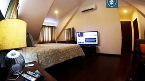 A hotel room with a bed, a TV, a lamp, and a remote control on a wooden nightstand. - Elite Hotel (Port-au-Prince)