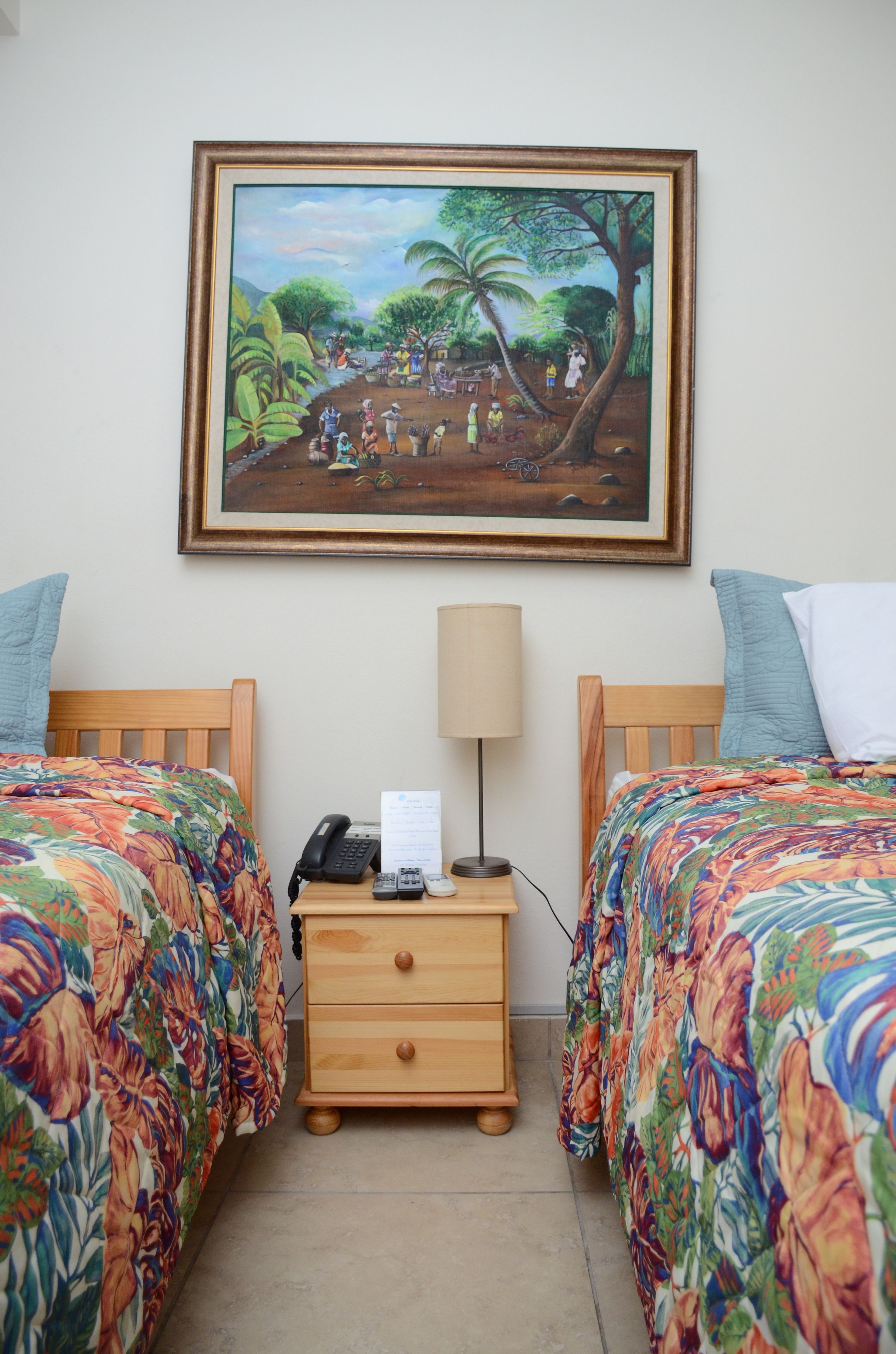 A hotel room with two beds, a nightstand with a lamp, a painting on the wall, and a telephone.