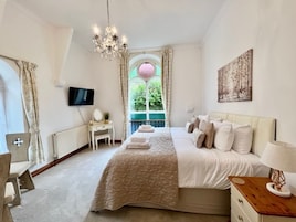 Un dormitorio con una cama grande, una mesita de noche con lámpara, un televisor en la pared y una ventana con cortinas.