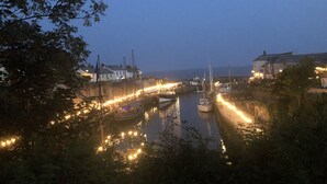A riverside town at dusk with boats docked along the water, buildings lining the riverbank, and streetlights illuminating the area. - The Chapel Guest House (St Austell)