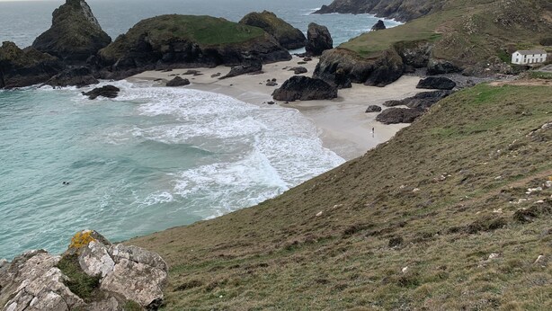 A coastal landscape with rocky outcrops, a sandy beach, and a grassy hill. - The Chapel Guest House (St Austell)