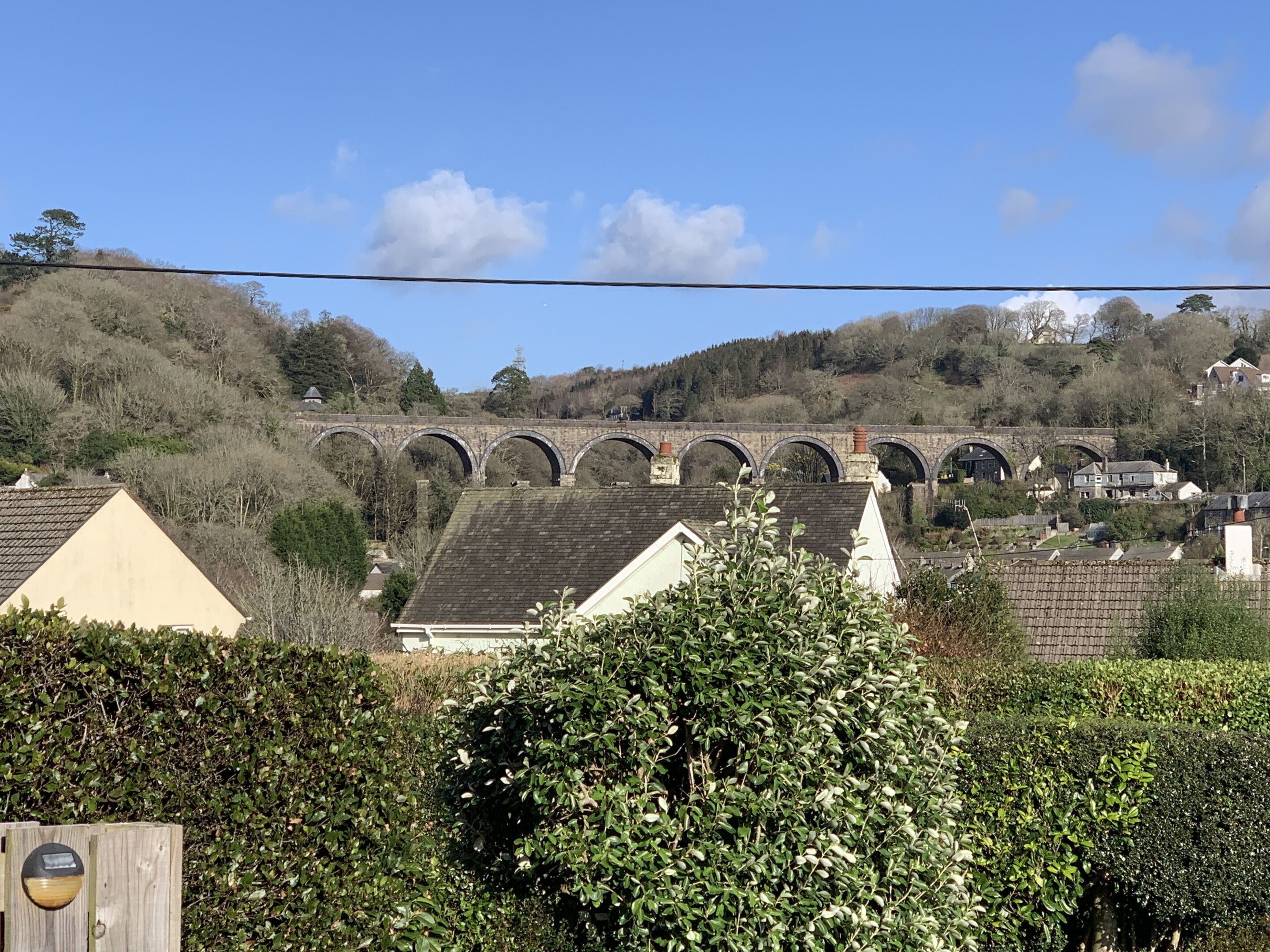 Ein Wohngebiet mit Häusern, einer Steinbrücke und einem Hügel mit Bäumen.