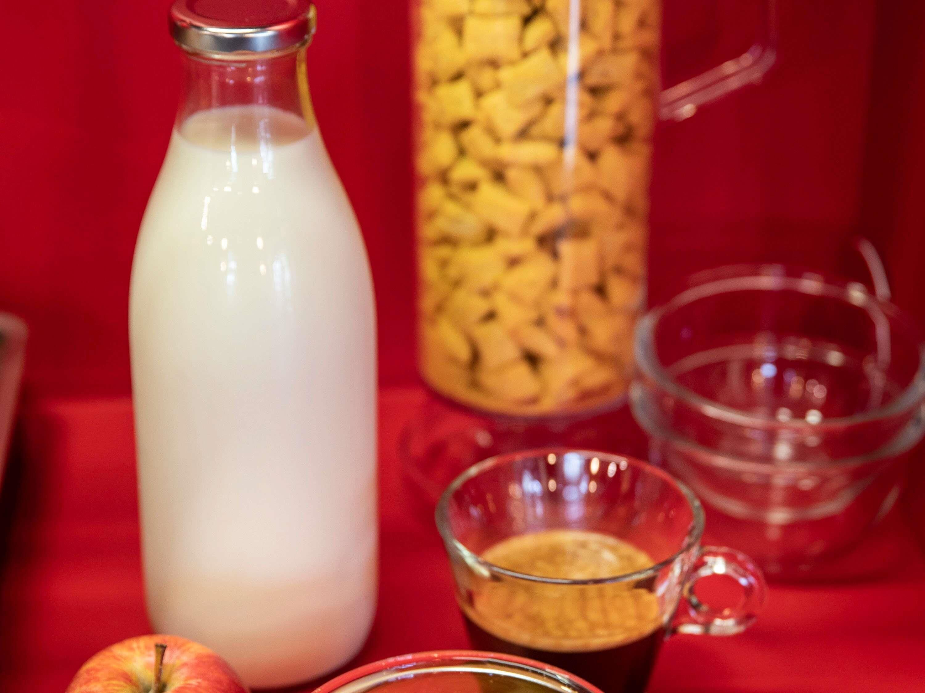 A glass bottle, a glass mug, a glass bowl, and an apple on a red surface.