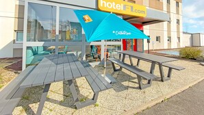A modern hotel with a yellow sign, outdoor seating, and a gravel patio. - hotelF1 Avranches Baie du Mont Saint Michel (Saint-Quentin-sur-le-Homme)