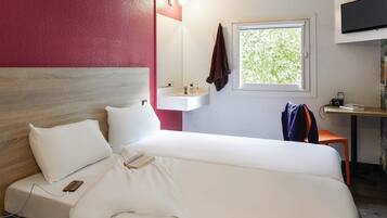 Una habitación de hotel con cama, mesita de noche, televisión, ventana y lavamanos.