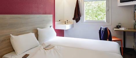 Una habitación de hotel con cama, mesita de noche, televisión, ventana y lavamanos.
