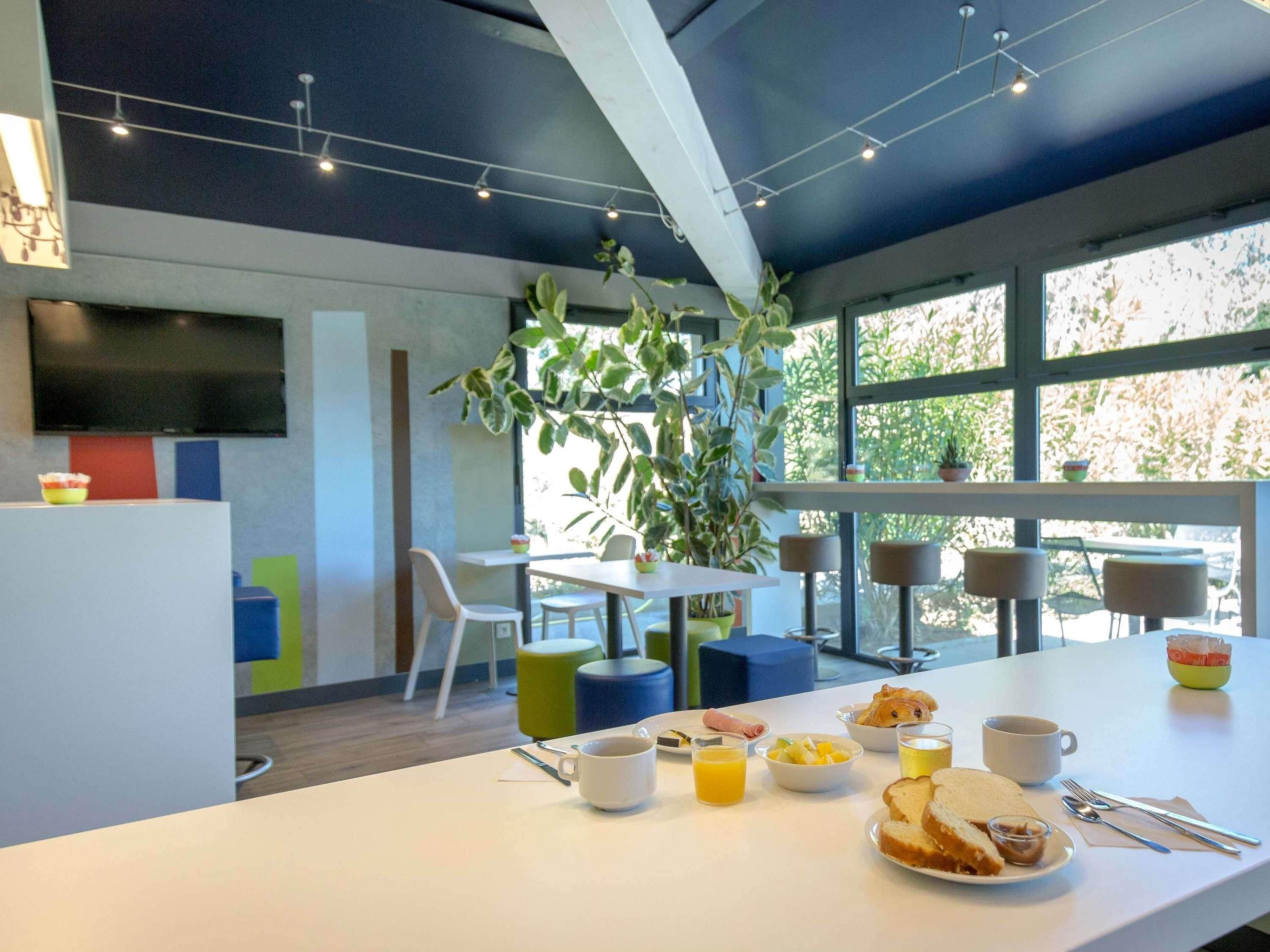 Un moderno comedor con una mesa blanca dispuesta para el desayuno, incluyendo pan, fruta y una taza de café.