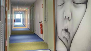 A hotel corridor with a fire extinguisher mounted on the wall, a fire alarm, and a door at the end.
