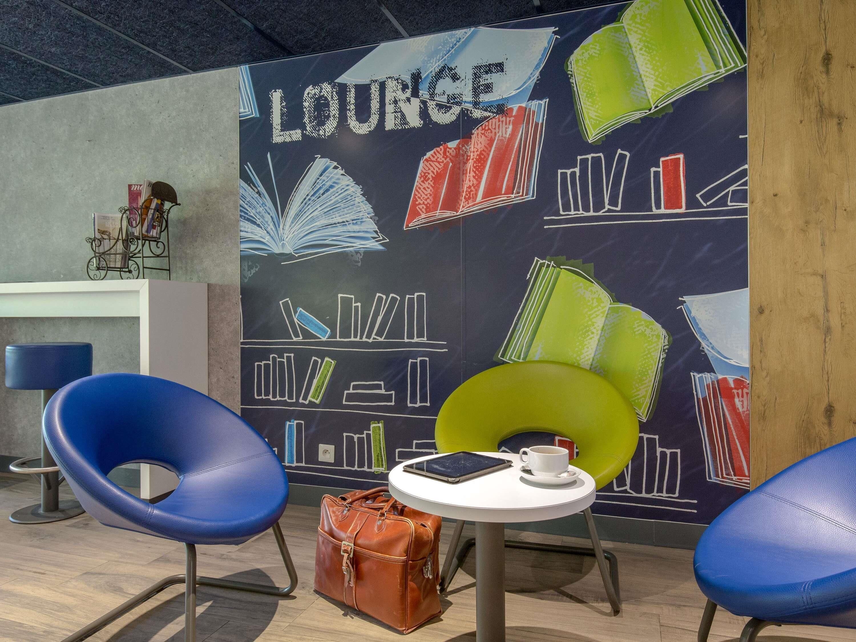 A lounge area with a wall mural, two blue chairs, a small white table, and a brown leather bag.