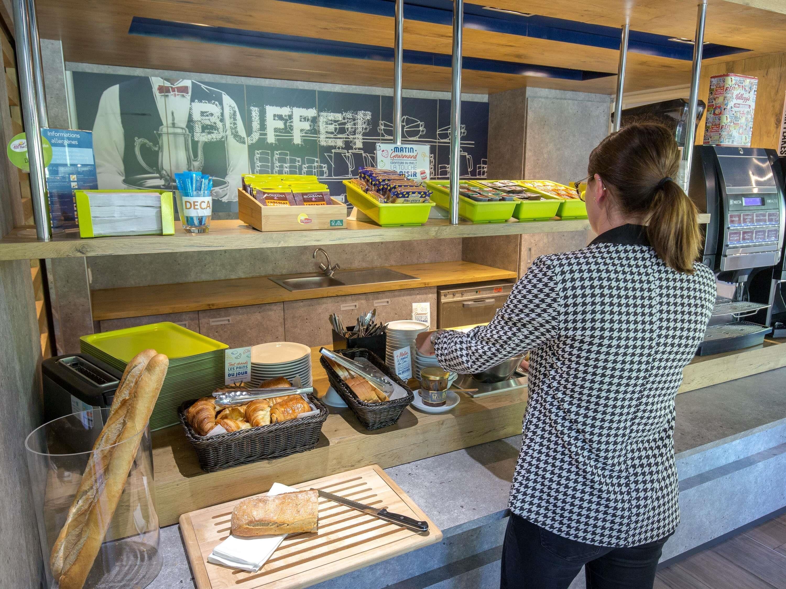Un comptoir de buffet proposant divers plats, une machine à café et une personne préparant de la nourriture.