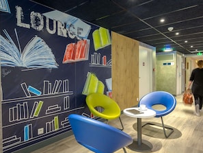 A lounge area with a wall mural, a wooden partition, and seating with a table. - ibis budget Brignoles Provence Verte (Brignoles)