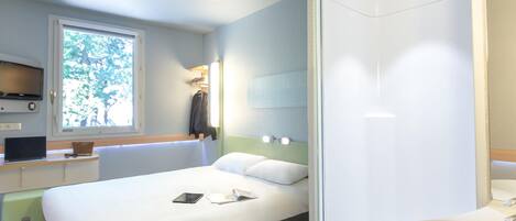 A modern hotel room with a bed, bedside table, TV, and a bathroom with a sink and mirror.