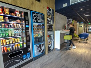A vending machine with snacks and drinks, a counter with a sign, and a person walking by. - ibis budget Brignoles Provence Verte (Brignoles)
