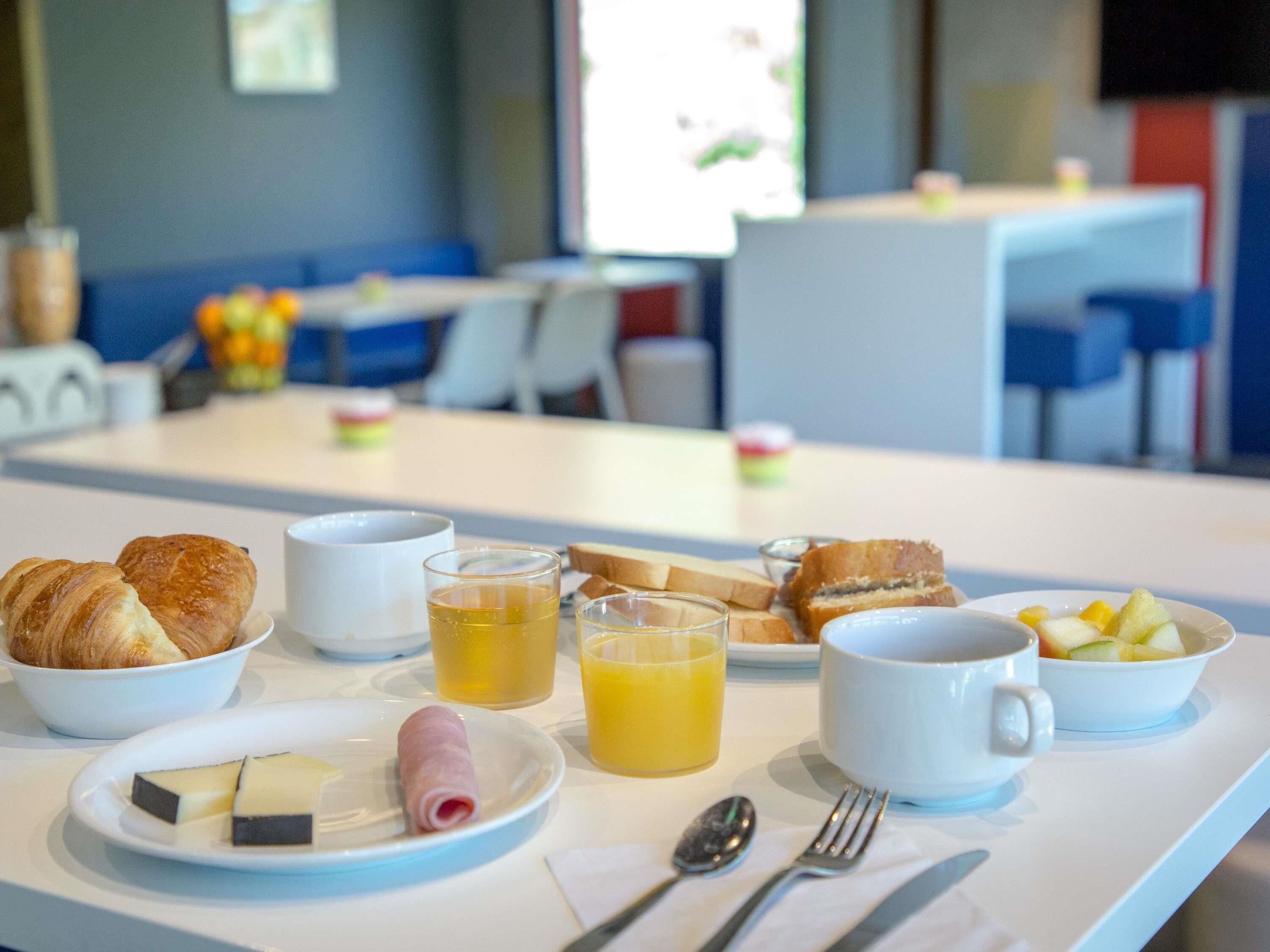Una mesa de desayuno con cruasanes, queso, jamón, jugo y fruta.