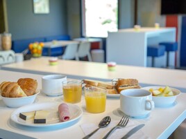 Una mesa de desayuno con cruasanes, queso, jamón, jugo y fruta.
