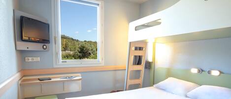A compact hotel room with a bed, a small desk with a TV, a window with a view, and a ladder.