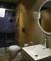 Un baño con ducha envuelta en vidrio, inodoro blanco y lavamanos con espejo.