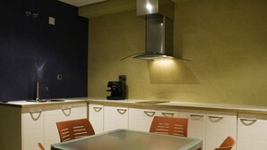 Une cuisine compacte avec une table à plateau en verre et quatre chaises, une machine à café et une hotte aspirante en acier inoxydable.