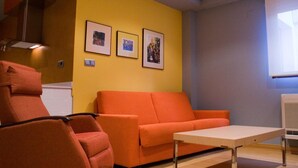 Une pièce avec un mur jaune, un canapé rouge, un fauteuil rouge et une petite table. Trois tableaux encadrés sont accrochés au mur.
