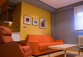 Una habitación con pared amarilla, sofá rojo, sillón rojo y una mesita pequeña. Hay tres cuadros enmarcados en la pared.