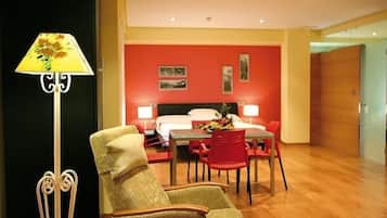 A hotel room with a bed, a dining table with chairs, a lamp, and a chair.