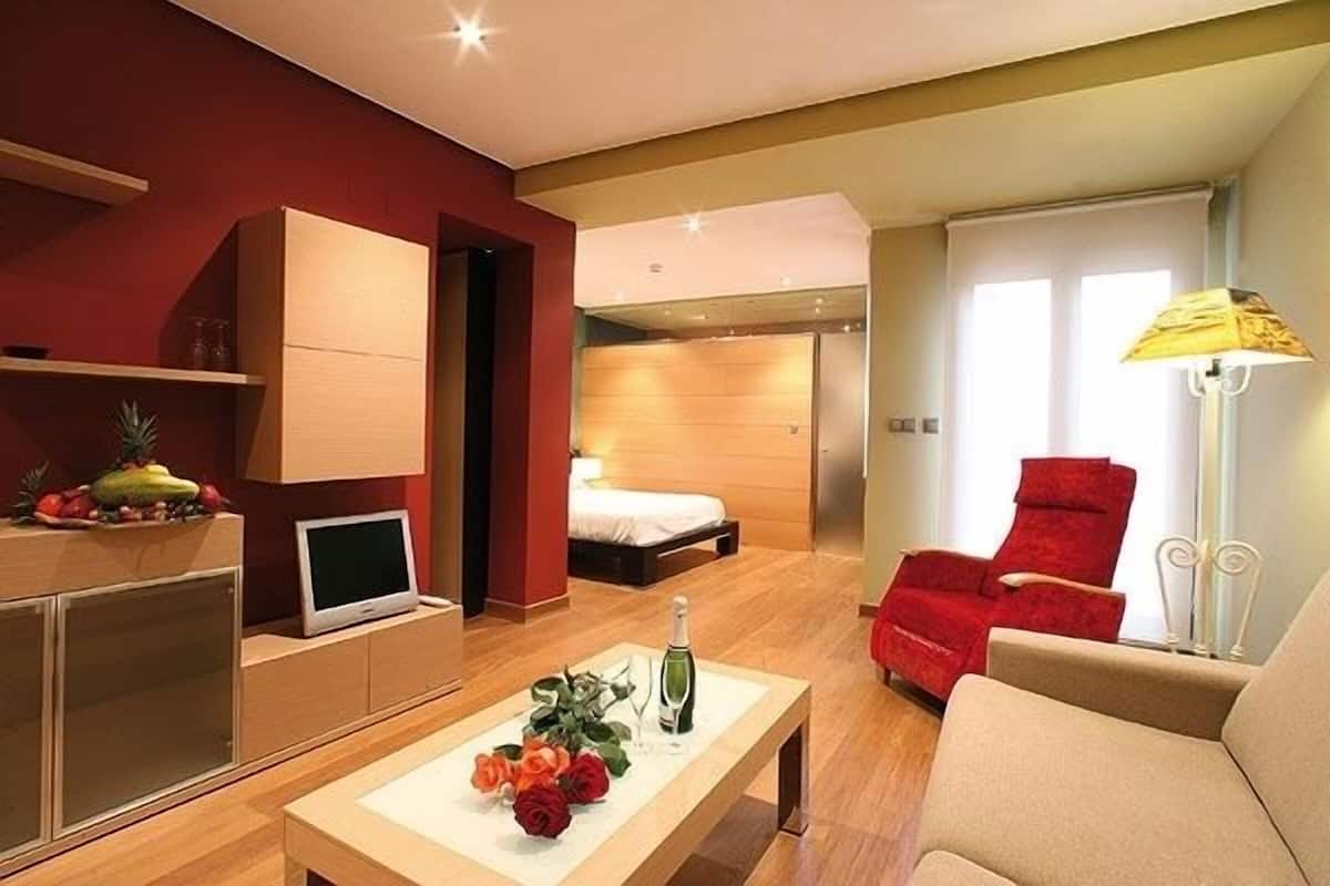 Ein modernes Hotelzimmer mit einem Bett, einem roten Sessel, einem Fernseher und einem Tisch mit Blumen.