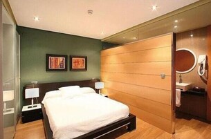 Un dormitorio moderno con cama, mesitas de noche, un espejo y un baño con lavamanos.