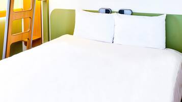 Cama com roupa de cama branca, cabeceira verde e dois relógios de cabeceira.