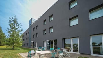 Un edificio moderno con techo plano, ventanas amplias y un patio con mobiliario exterior.