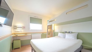 A hotel room with a bed, a desk, a chair, a window, and a television.