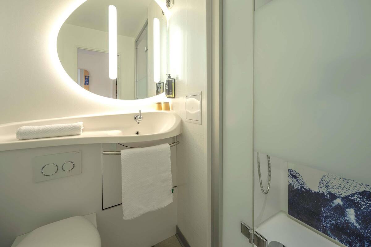 A modern bathroom with a round mirror, a white sink, and a glass shower enclosure.
