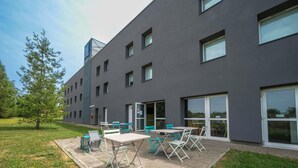 A modern building with a flat roof, large windows, and a patio area with outdoor seating.