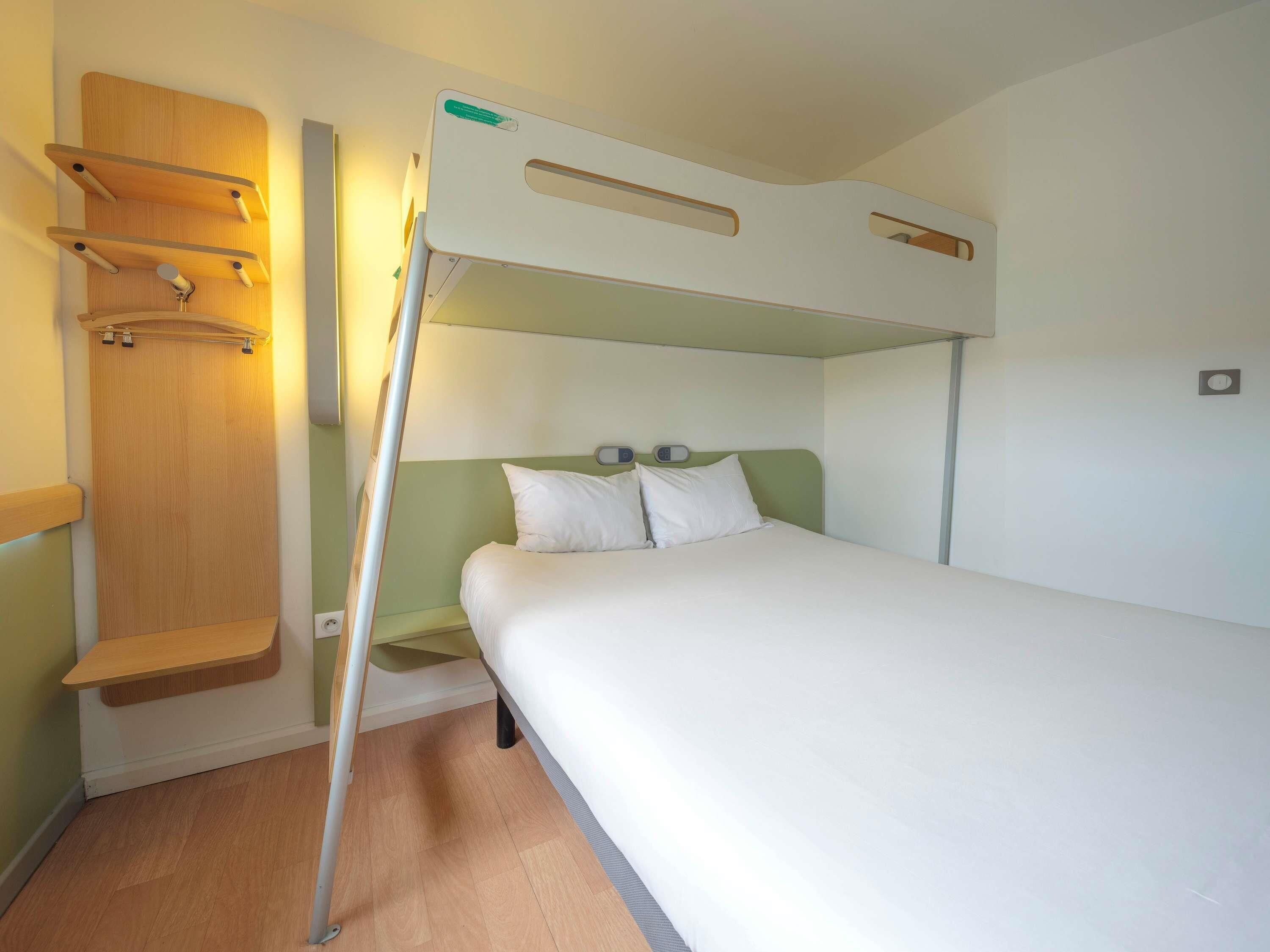 A bunk bed with a wooden shelf above, a bedside table, and a wall-mounted thermostat.