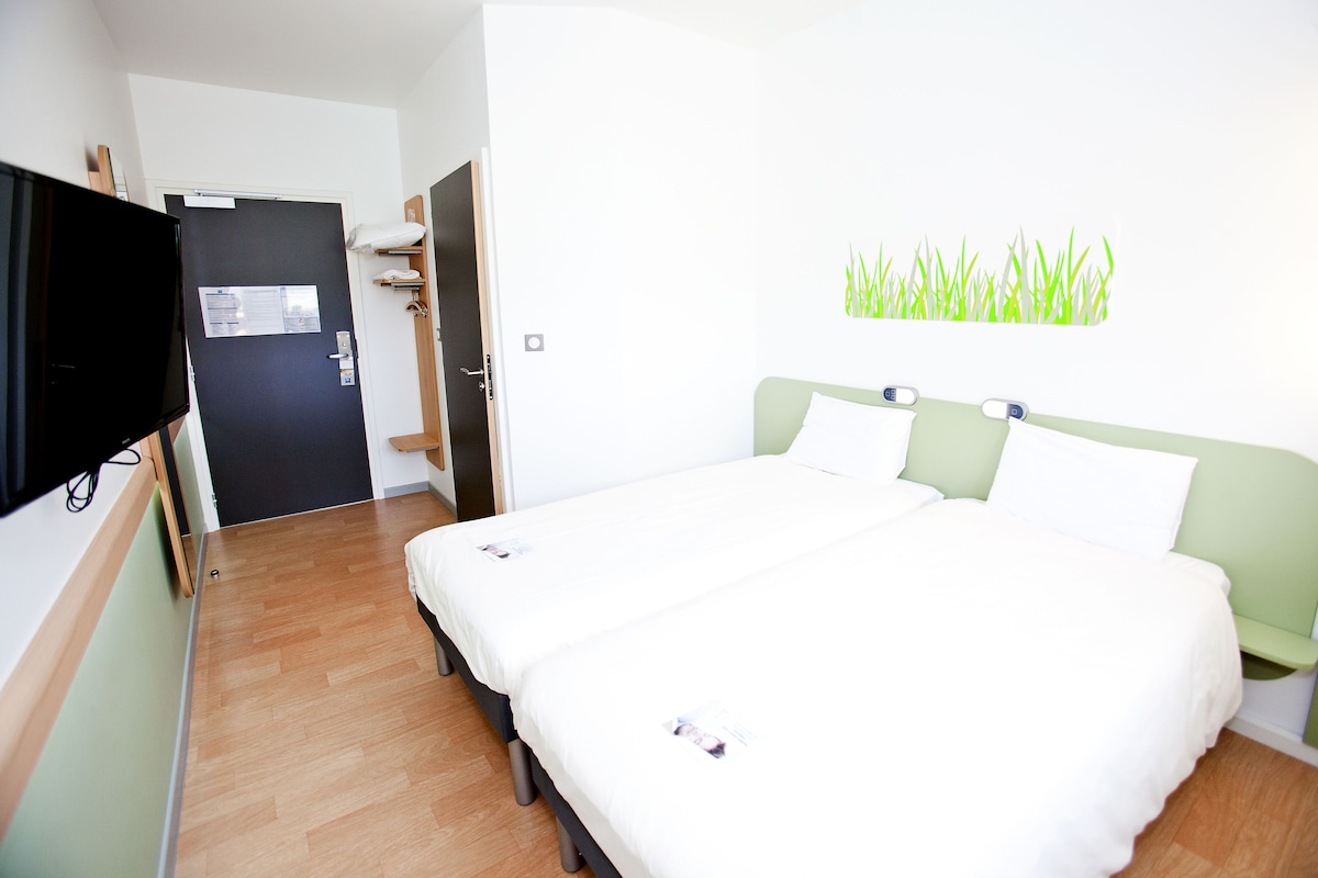 A hotel room with a bed, a TV, and a door leading to a bathroom.