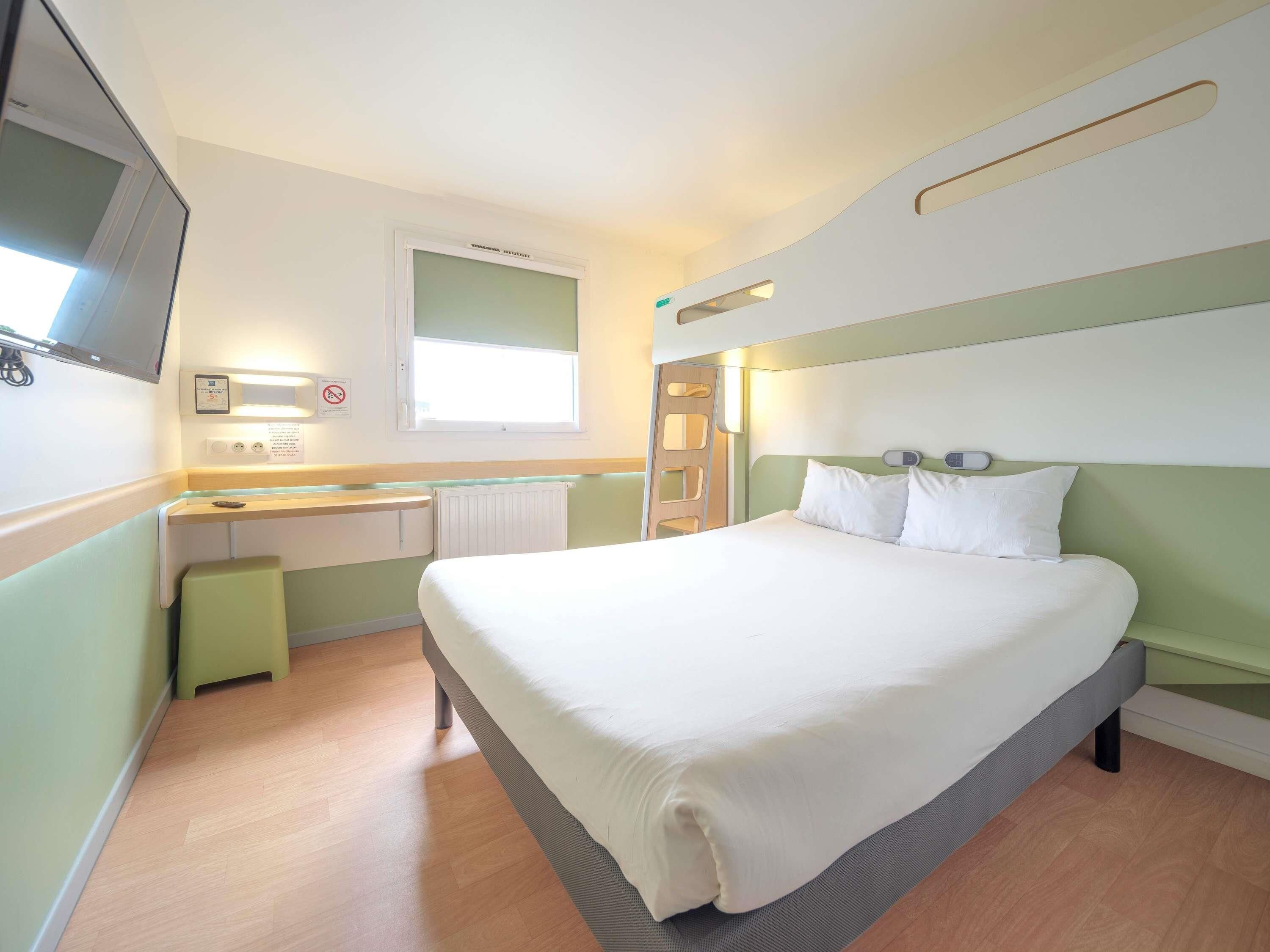 A hotel room with a bed, a desk, a chair, a window, and a television.