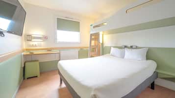 A hotel room with a bed, a desk, a chair, a window, and a television.