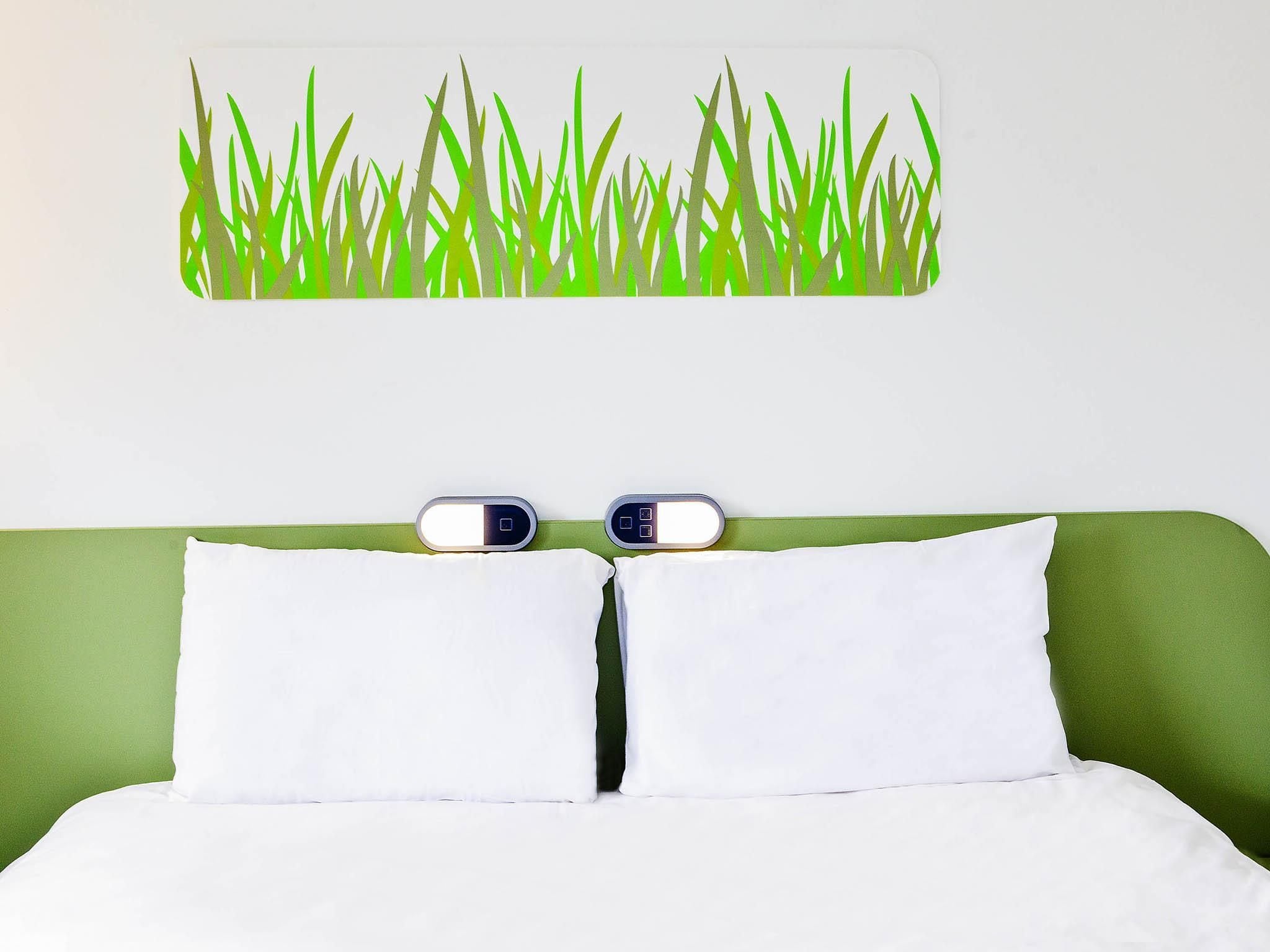 Een bed met witte beddengoed, een groen hoofdbord en twee nachtklokken.