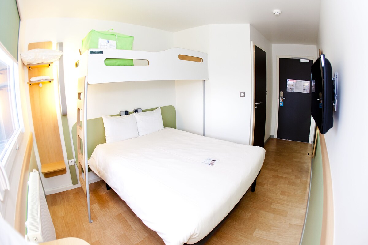 A bunk bed room with a white bed, a green pillow, and a wooden shelf.