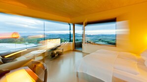 Habitació d'hotel moderna amb un llit gran, un escriptori amb un ordinador i una televisió. L'habitació té grans finestres que ofereixen vistes al camp rural.