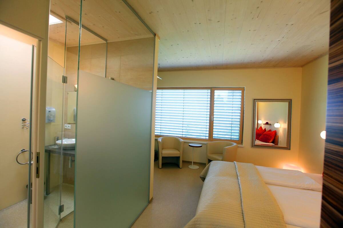A hotel room with a bed, a desk, a chair, and a large window with blinds.