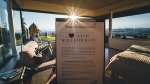 Habitació d'hotel moderna amb una finestra gran, vistes plenes de sol, zona de seients acollidora i un cartell de benvinguda.
