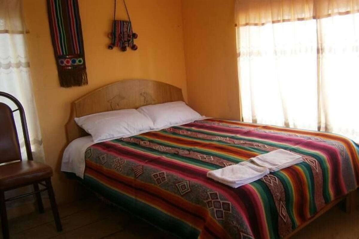 A bed with a colorful blanket, a wooden headboard, and a chair to the left.
