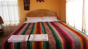A bed with a colorful striped bedspread and two neatly folded towels. - Samay Wasi Salakancha (Isla Amantani)