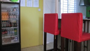 A room with a refrigerator stocked with beverages, a window with bars, and red chairs.
